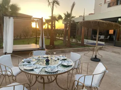 a table and chairs on a patio with the sunset at Hôtel Jardins de lina et lea in Marrakech