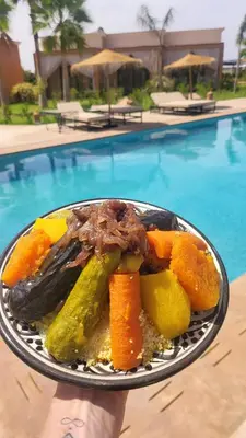 a plate of food on a table next to a pool at Hôtel Jardins de lina et lea in Marrakech