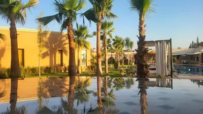 a pool with palm trees in front of a house at Hôtel Jardins de lina et lea in Marrakech
