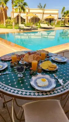 a table with breakfast food on it in front of a pool at Hôtel Jardins de lina et lea in Marrakech