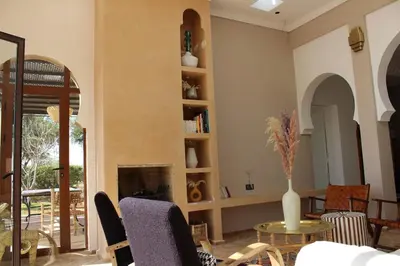 a living room with a fireplace and a table and chairs at Villa Ily Marrakech Oasis privée avec piscine chauffée et panorama Atlas in Marrakech